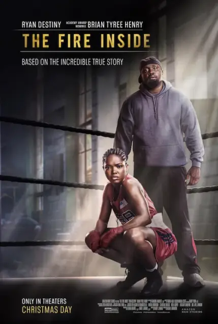 The Fire Inside (2024) Movie Poster. The movie poster features two individuals in a boxing ring. The person on the left is kneeling, wearing a red boxing outfit with the number "29" on it, and red boxing gloves. The person on the right is standing, dressed in a gray hoodie and black pants, with a serious expression. The background is dimly lit, with a focus on the boxing ring and the two individuals. The text at the top of the poster reads "THE FIRE INSIDE" in bold, yellow letters, and below it, it states "BASED ON THE INCREDIBLE TRUE STORY." At the bottom, it mentions "ONLY IN THEATERS CHRISTMAS DAY" and credits the production companies involved.