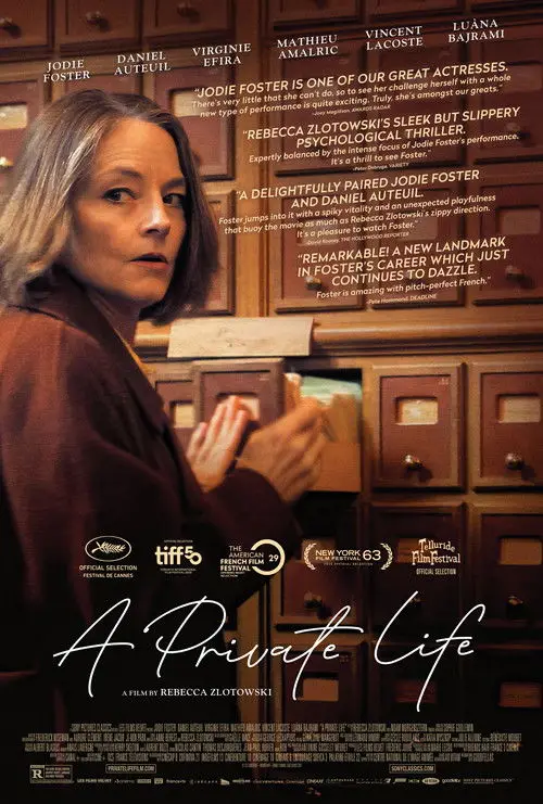 A Private Life (2025) - Movie Poster. The movie poster features a woman with short, light-colored hair, wearing a brown jacket, standing in front of a wooden cabinet with multiple drawers. The cabinet has a rustic appearance with visible wood grain and metal handles. The woman is holding a small object in her hand, which appears to be a piece of paper or a card. The background is a mix of warm tones, predominantly brown and beige, creating a cozy and somewhat mysterious atmosphere. The title of the movie, "A Private Life," is prominently displayed at the bottom in a stylized font. Above the title, there are several quotes praising the film, mentioning Jodie Foster, Daniel Auteuil, and other actors. The poster also includes logos for various film festivals, indicating the film's selection and recognition at these events.
