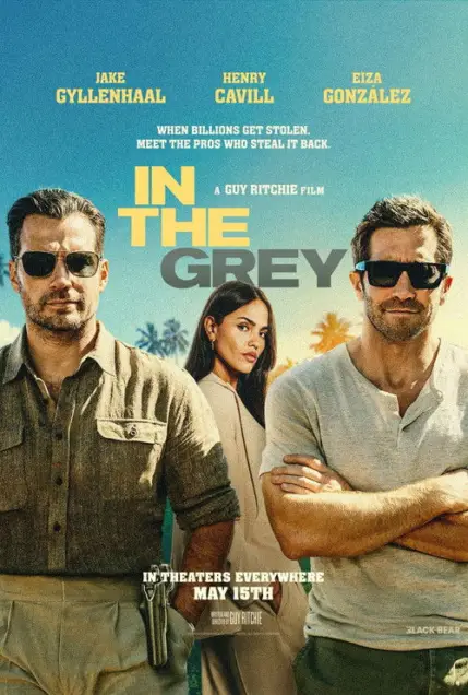 In the Grey (2026) - Movie Poster. The movie poster features three individuals prominently. On the left, a man with a beard and sunglasses is wearing a dark shirt and pants, with a gun holstered at his side. In the center, a woman with long hair is dressed in a light-colored outfit, looking directly at the viewer. On the right, another man with a beard and sunglasses is wearing a light-colored shirt and pants, with his arms crossed. Above them, the names "Jake Gyllenhaal," "Henry Cavill," and "Eiza González" are listed, indicating the main actors. The title "In The Grey" is displayed in bold, yellow letters, with a tagline below it that reads, "When billions get stolen, meet the pros who steal it back." The poster also includes the release date, "In theaters everywhere May 15th," and credits "A Guy Ritchie Film." The background is a gradient of blue and green, suggesting an outdoor setting.