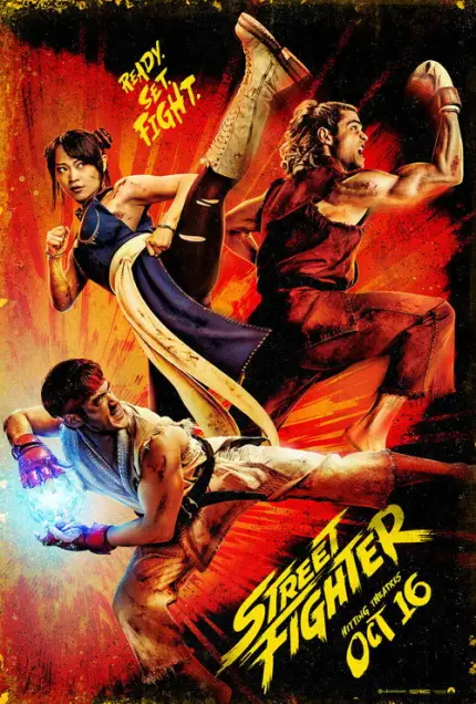Street Fighter (2026) - Movie Poster. The movie poster features three characters engaged in dynamic combat poses against a vibrant, fiery background. The character on the left is a woman with a determined expression, wearing a blue outfit and kicking with her right leg extended. The central character is a man with long hair, dressed in a red outfit, and appears to be in a defensive stance with his arms raised. The character on the right is a man lying on the ground, wearing a white outfit, and holding a glowing object in his hand. The text on the poster reads "Ready. Set. Fight." at the top and "Street Fighter" with the release date "Oct 16" at the bottom. The overall design conveys a sense of action and excitement.